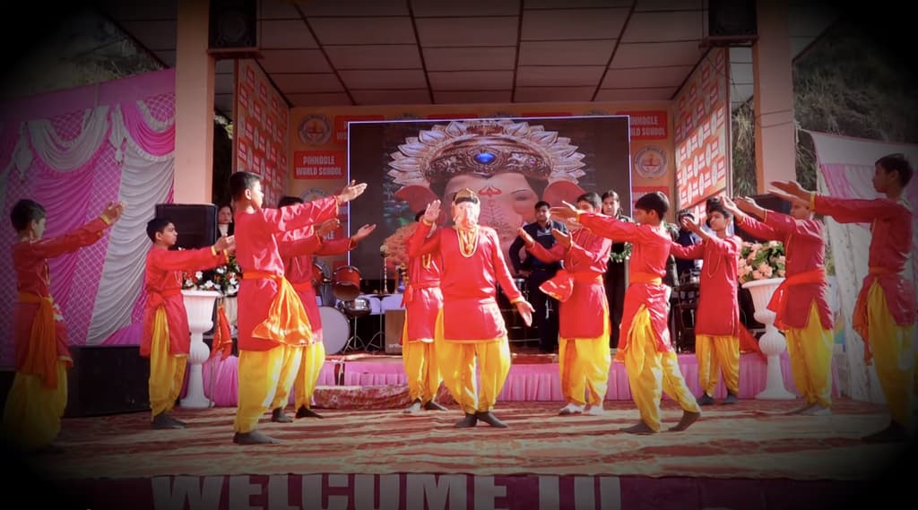 Students in red and yellow costumes dance in front of a Ganesha backdrop