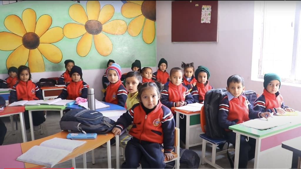 Young students in red school jackets at their desks, below a painted flower mural